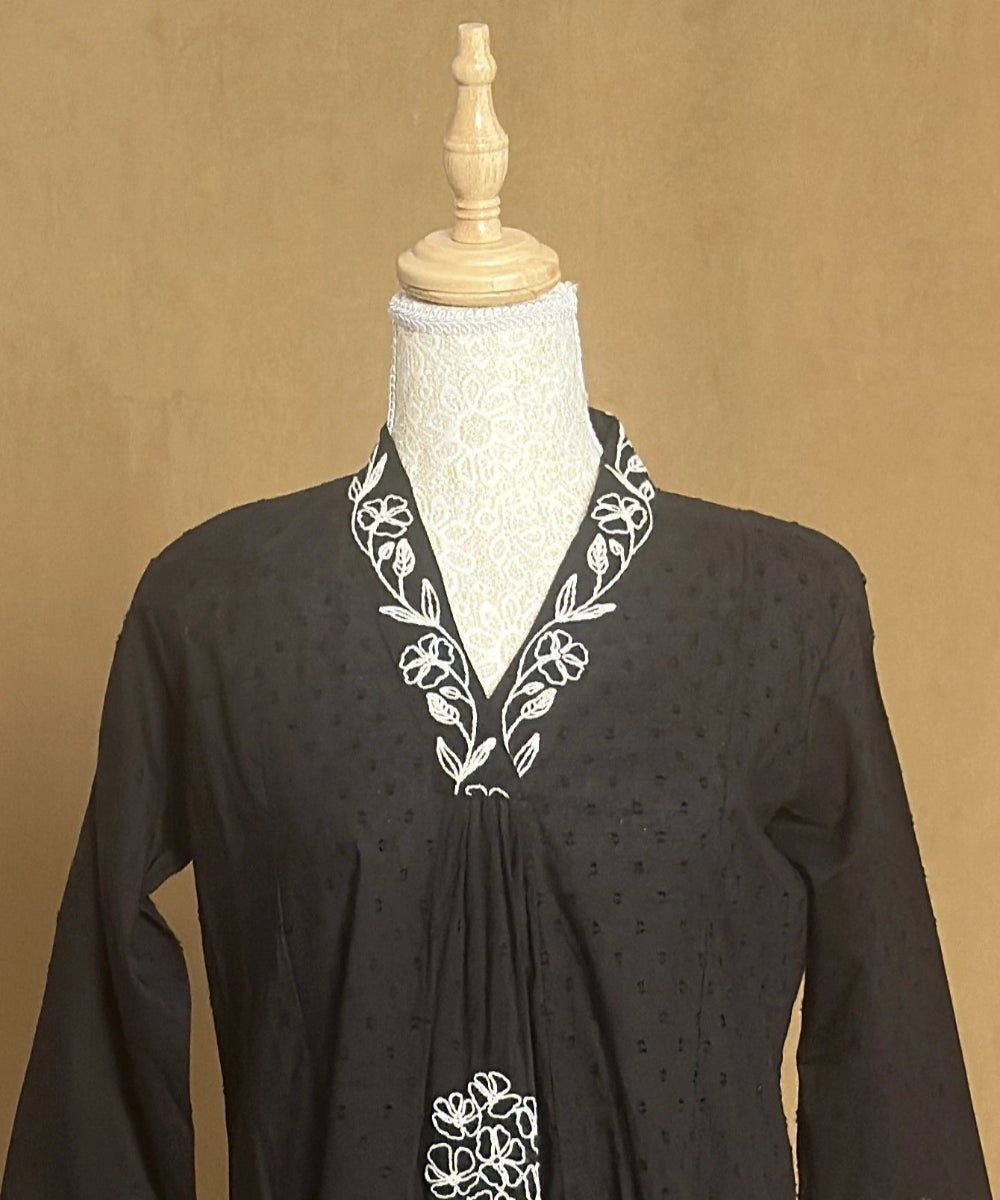 Black dress with white embroidery on a mannequin against a beige background