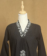 Black dress with white embroidery on a mannequin against a beige background