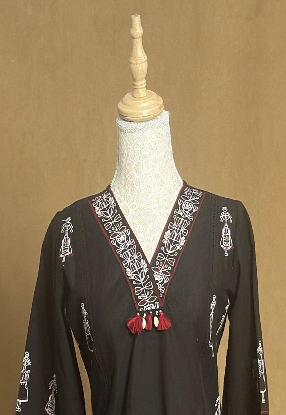 Black dress with intricate white embroidery on a mannequin against a brown background