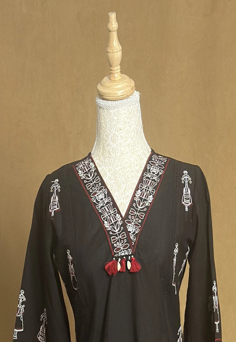 Black dress with intricate white embroidery on a mannequin against a brown background
