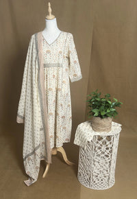 Long floral dress on a mannequin with a small table and plant against a brown background