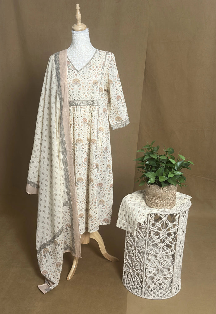 Long floral dress on a mannequin with a small table and plant against a brown background