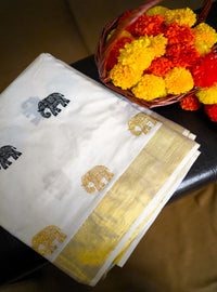 White saree with gold and black patterns on a table with marigold flowers.
