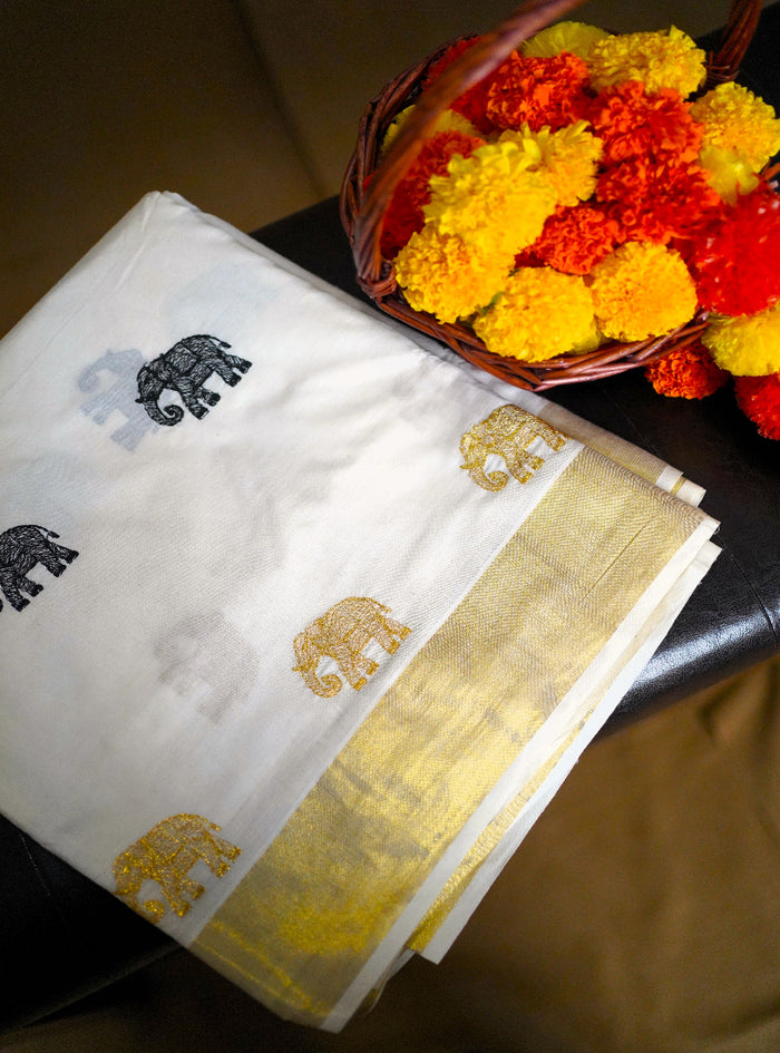 White saree with gold and black patterns on a table with marigold flowers.