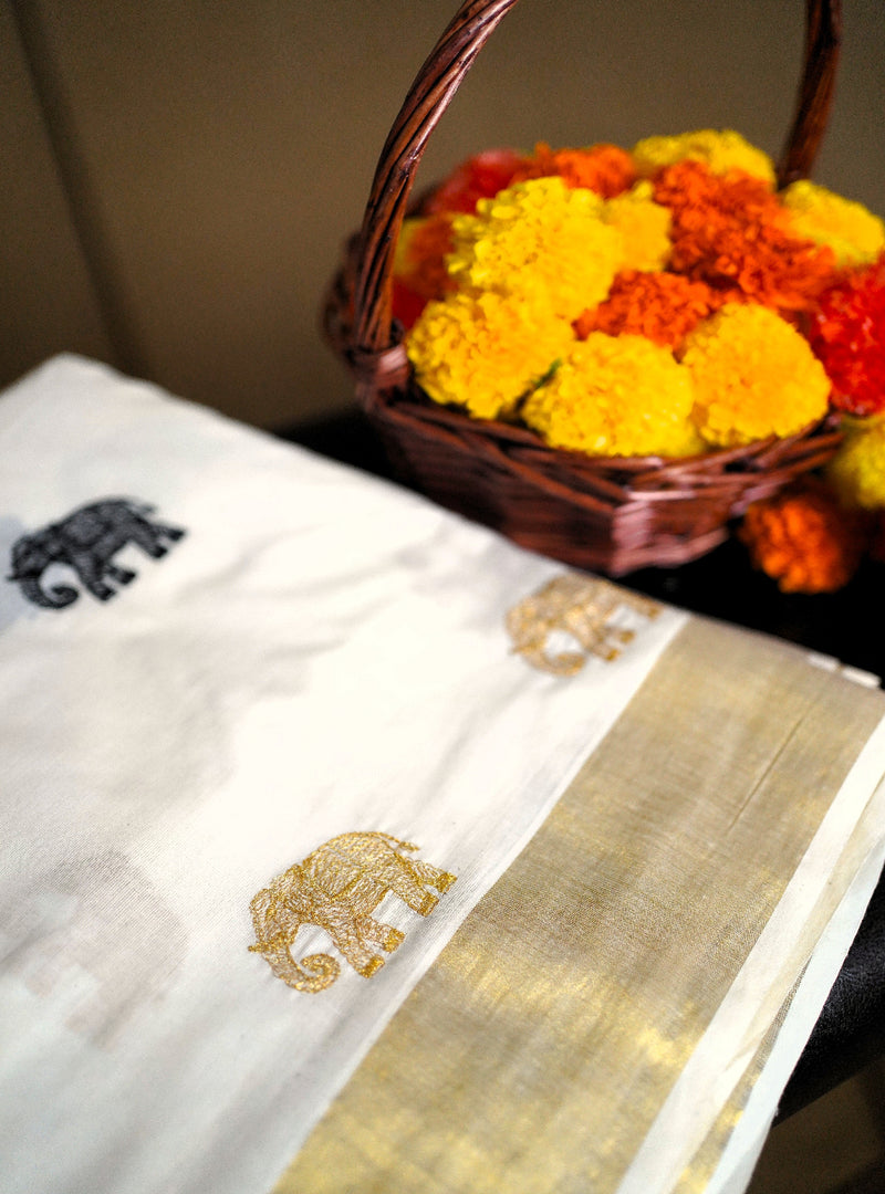 White saree with gold elephant design and marigold flowers in a basket.