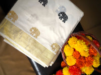 White saree with gold border and elephant patterns next to a basket of marigold flowers.