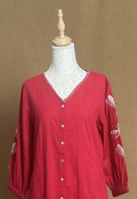 Red blouse with lace detailing on a mannequin against a brown background