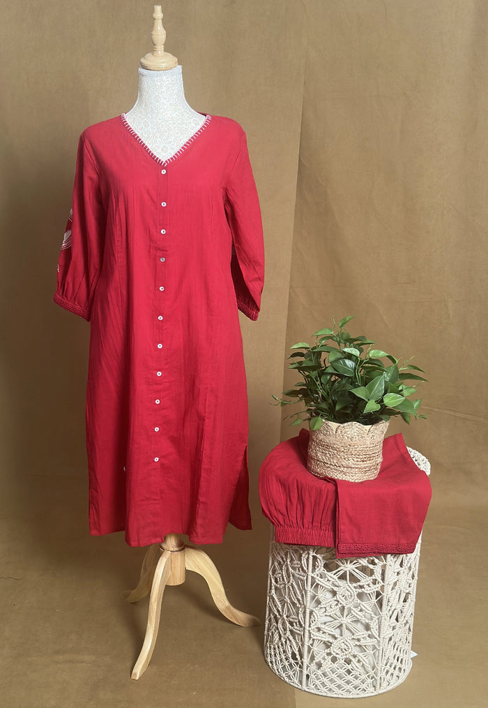 Red dress on a mannequin with a plant on a woven stool against a brown background