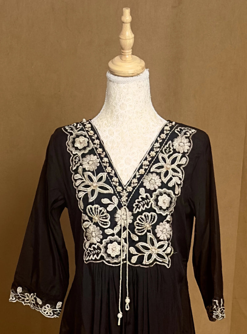 Black dress with white floral embroidery on a mannequin against a brown background