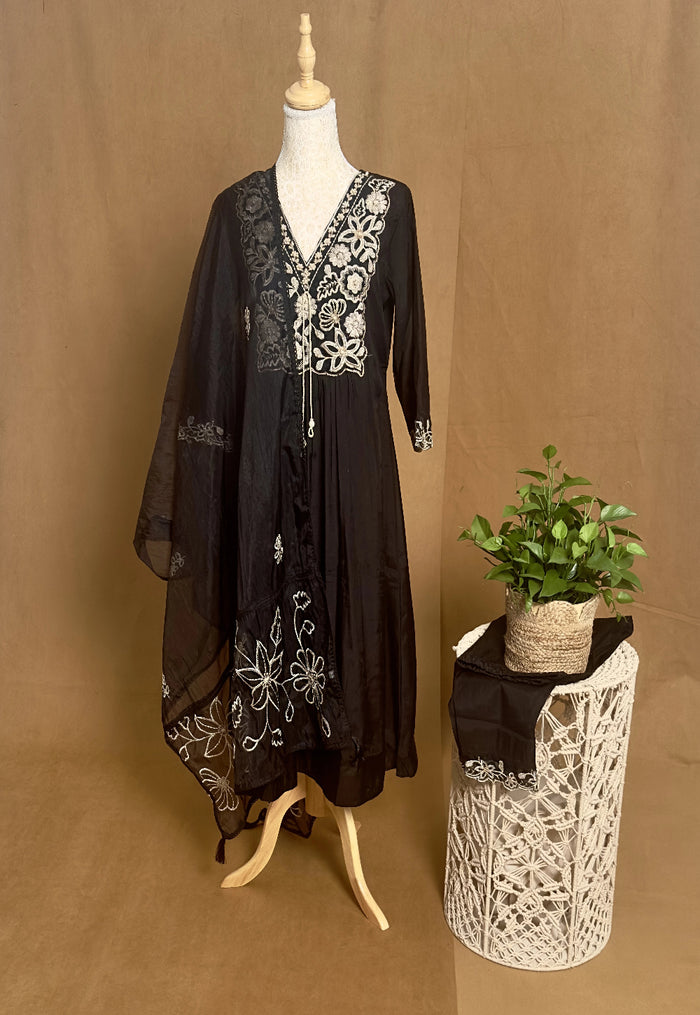 Black dress with white floral embroidery on a mannequin against a brown background