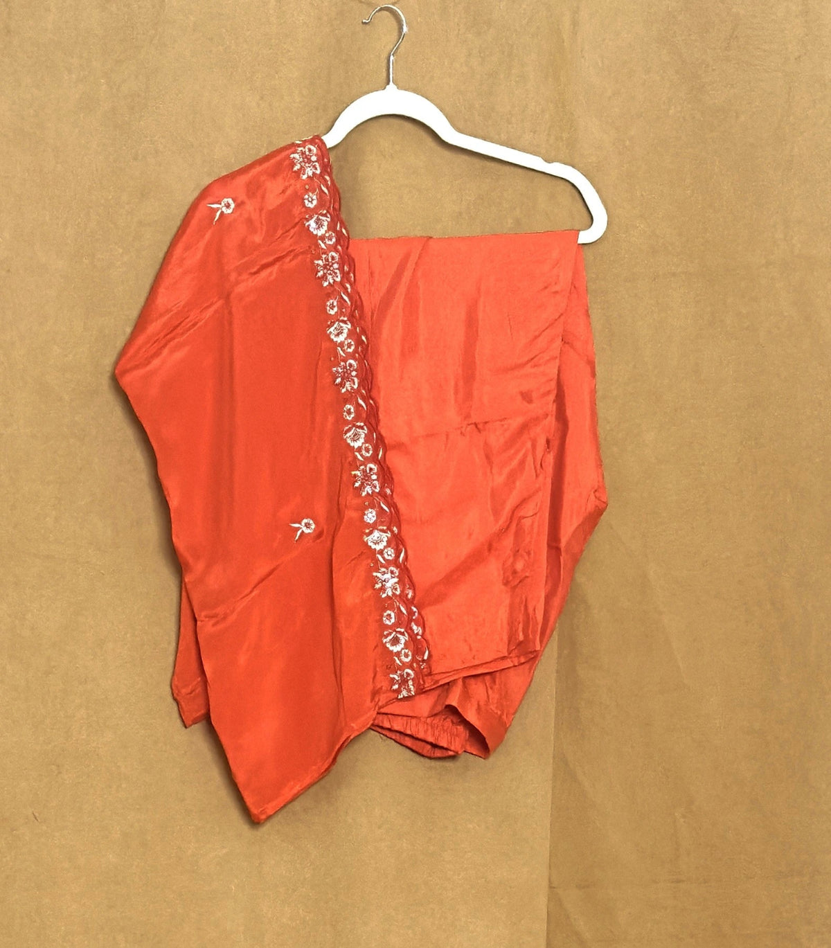  orange garment with floral embroidery on a white hanger against a brown background