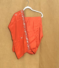  orange garment with floral embroidery on a white hanger against a brown background