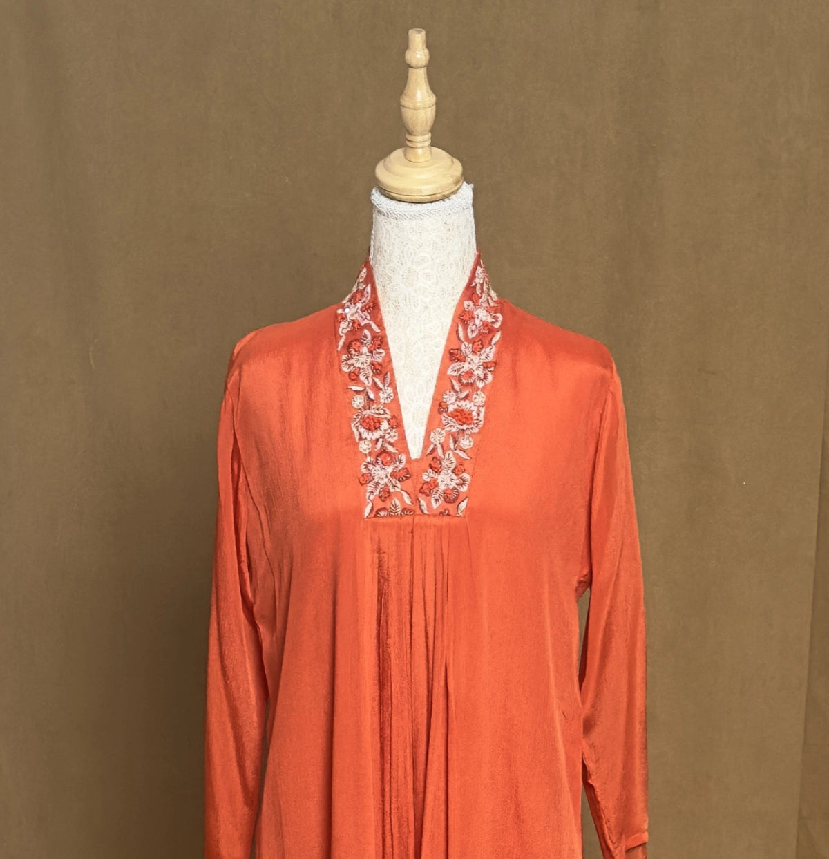 Orange long-sleeve top with floral embroidery on a mannequin against a brown background