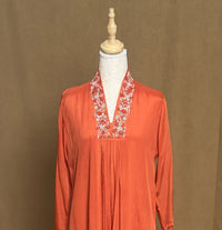 Orange long-sleeve top with floral embroidery on a mannequin against a brown background