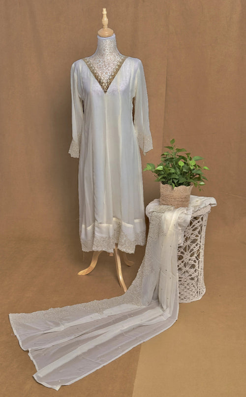 White lace anarkali on a mannequin with a plant on a small table against a brown background