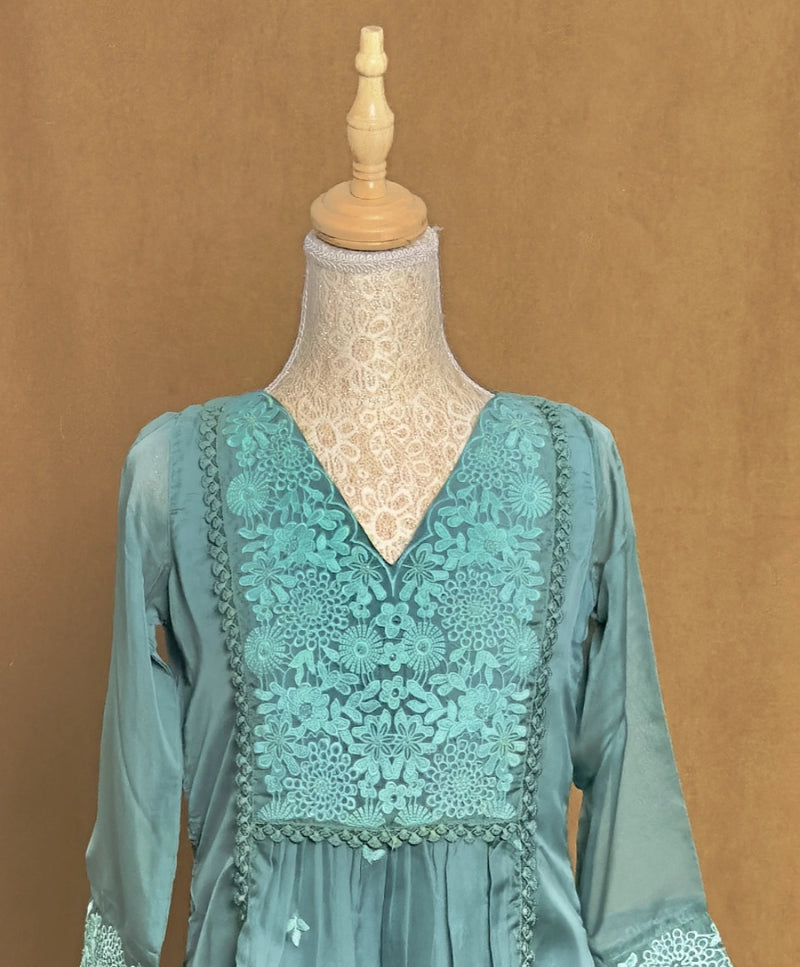 Teal dress with lace detailing on a mannequin against a brown background