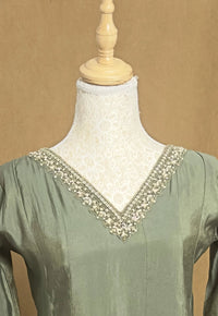 Green dress with intricate white embroidery on a mannequin against a beige background