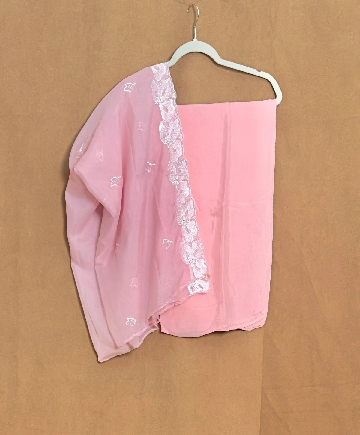 Pink scarf with white lace trim on a hanger against a brown background