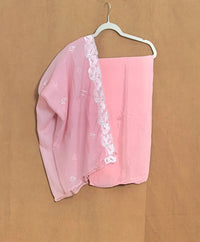 Pink scarf with white lace trim on a hanger against a brown background