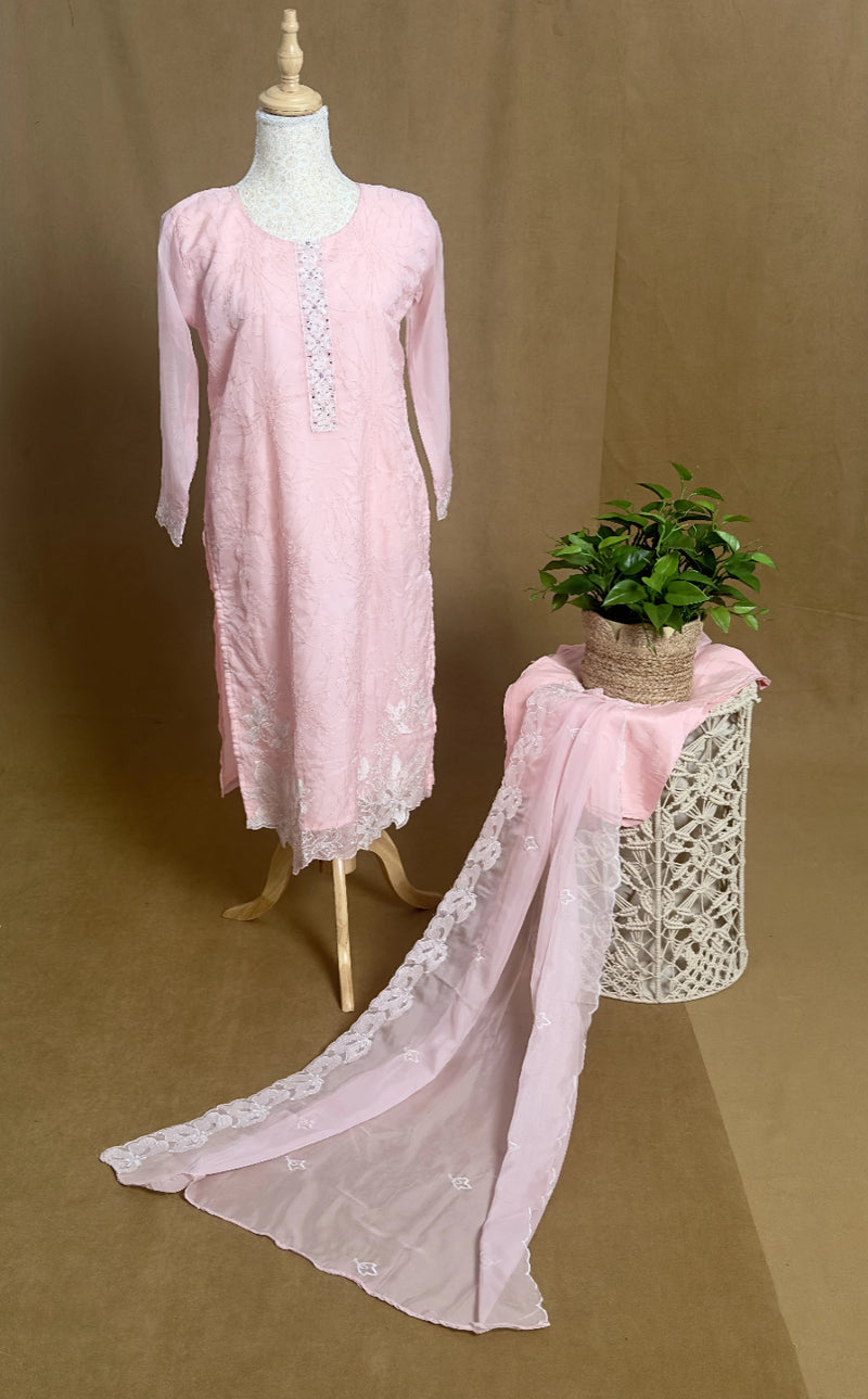 Pink lace dress on a mannequin with a matching scarf draped over a plant stand against a brown background