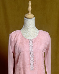 Pink blouse with lace detailing on a mannequin against a brown background