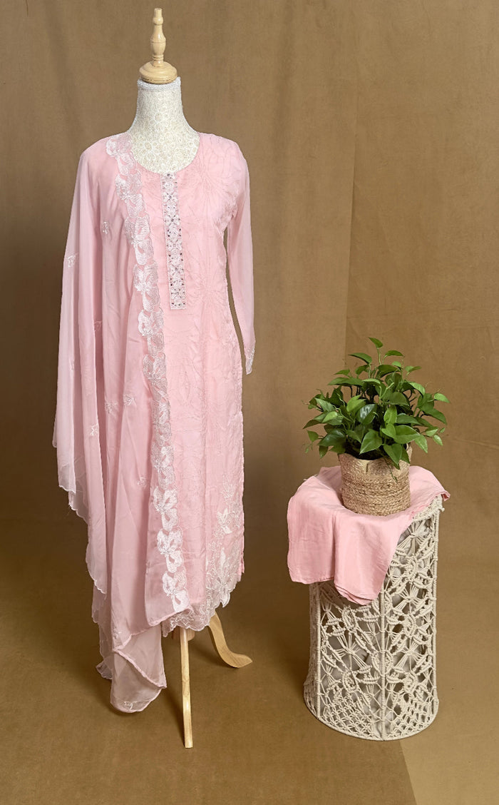 Pink lace dress on a mannequin with a plant on a stool against a brown background