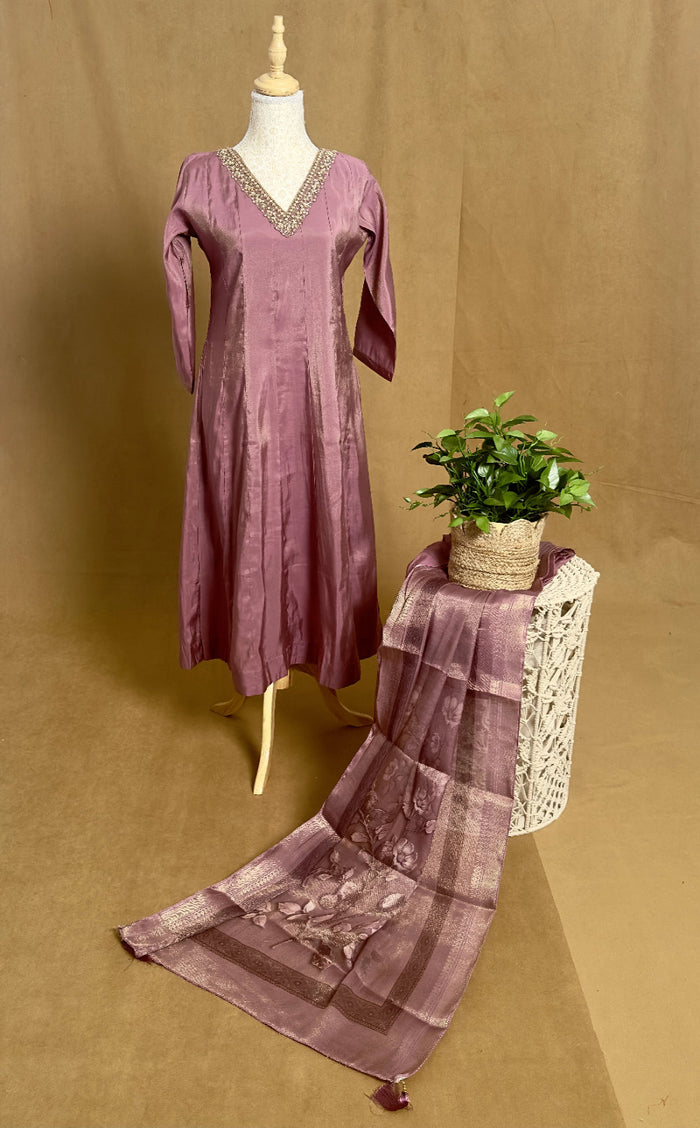 Purple dress on a mannequin with a matching scarf and plant on a table against a brown background