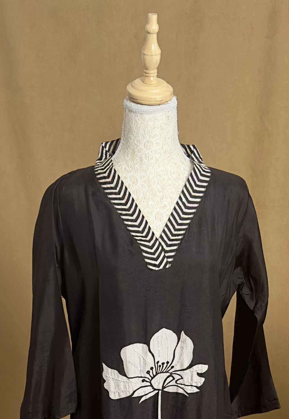 Black top with white floral design and striped collar on a mannequin against a brown background