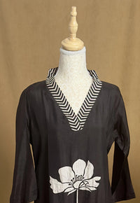 Black top with white floral design and striped collar on a mannequin against a brown background
