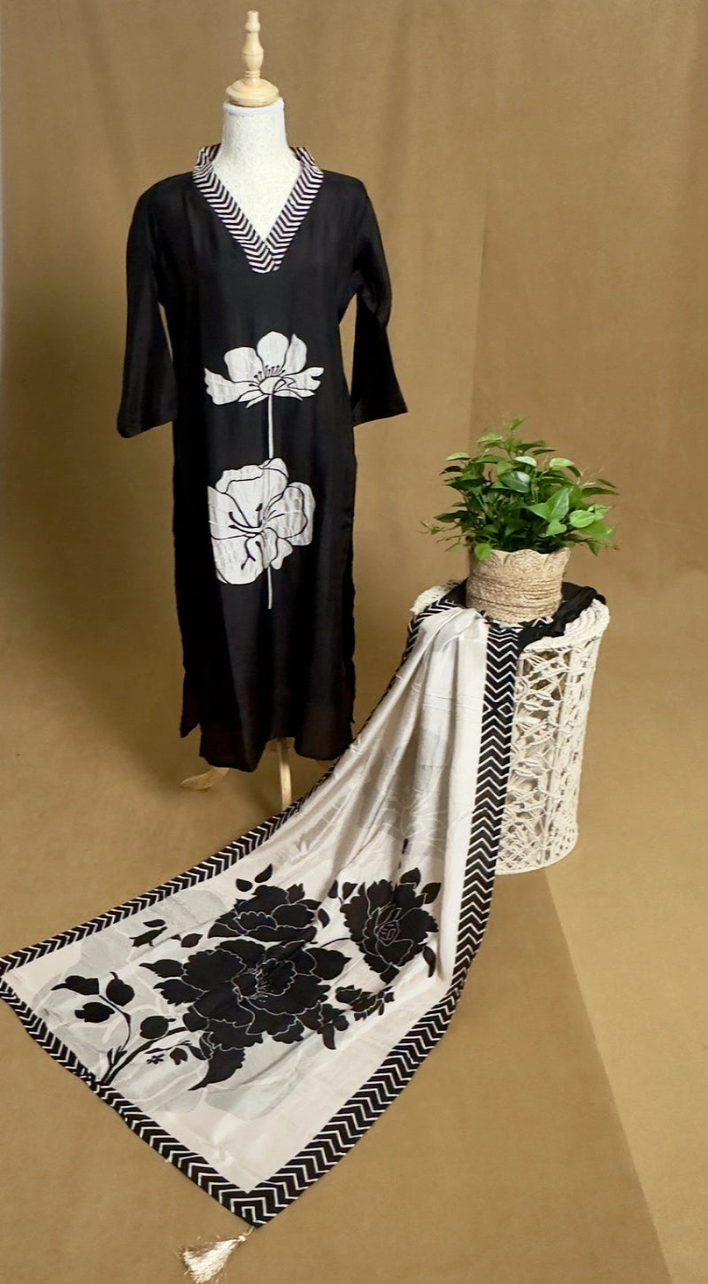 Black dress with white floral design on a mannequin, next to a matching scarf on a stand against a brown background.