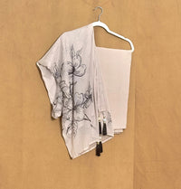 White scarf with black floral patterns and tassels on a hanger against a beige background
