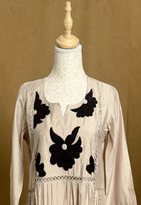 White dress with black floral embroidery on a mannequin against a beige background