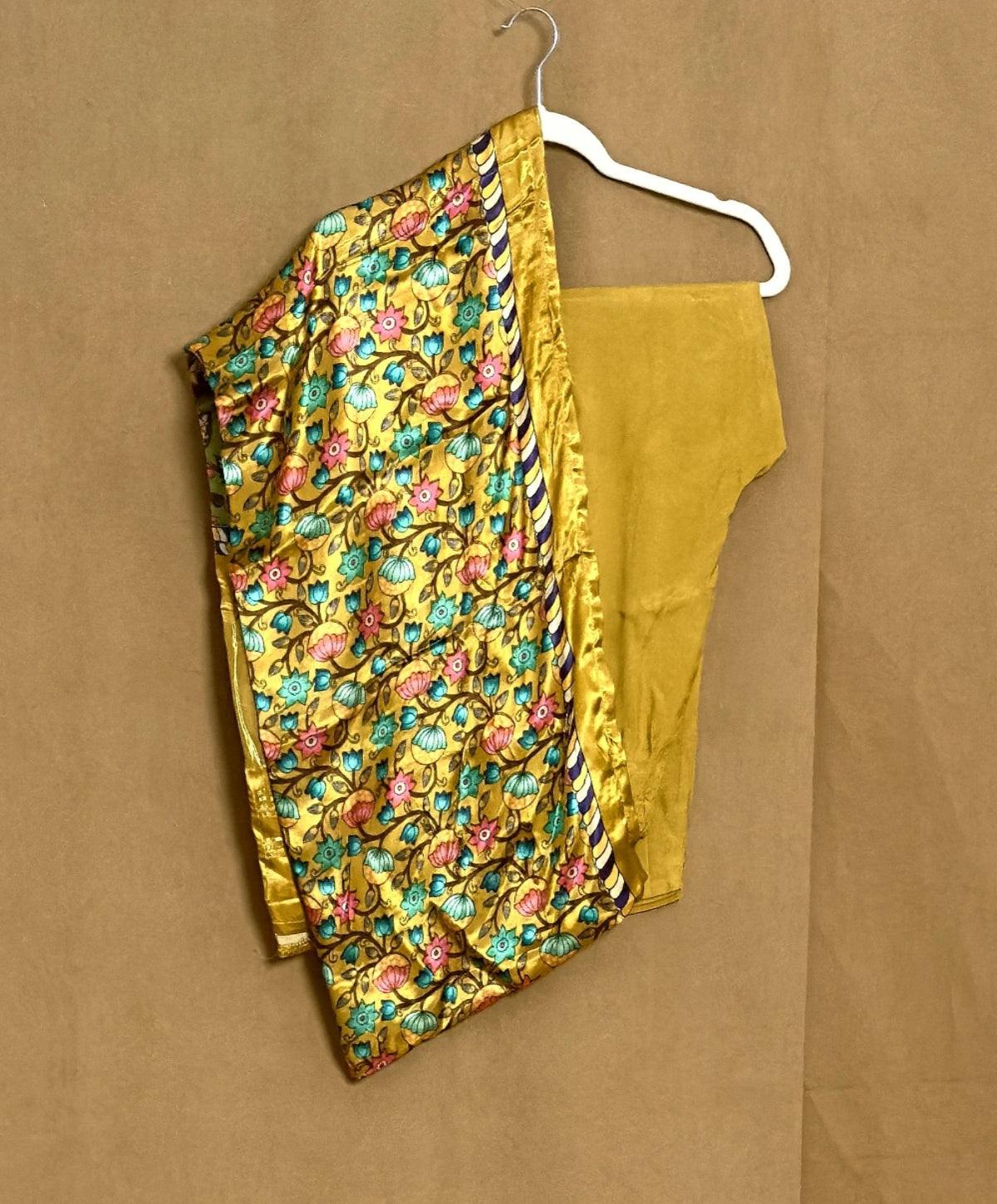 Yellow floral saree with a blouse piece on a hanger against a brown background