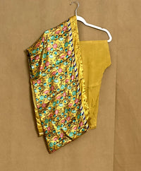 Yellow floral saree with a blouse piece on a hanger against a brown background