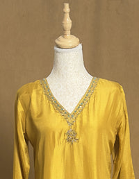 Yellow blouse with intricate embroidery on a mannequin against a brown background