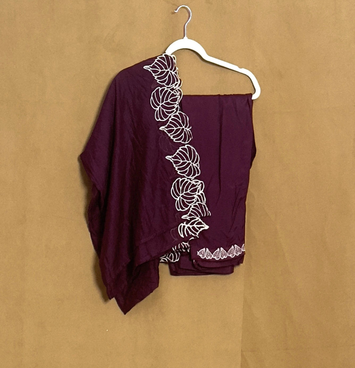 Maroon garment with white floral embroidery on a beige background