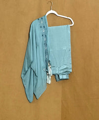 Teal outfit with a shawl on a hanger against a brown background