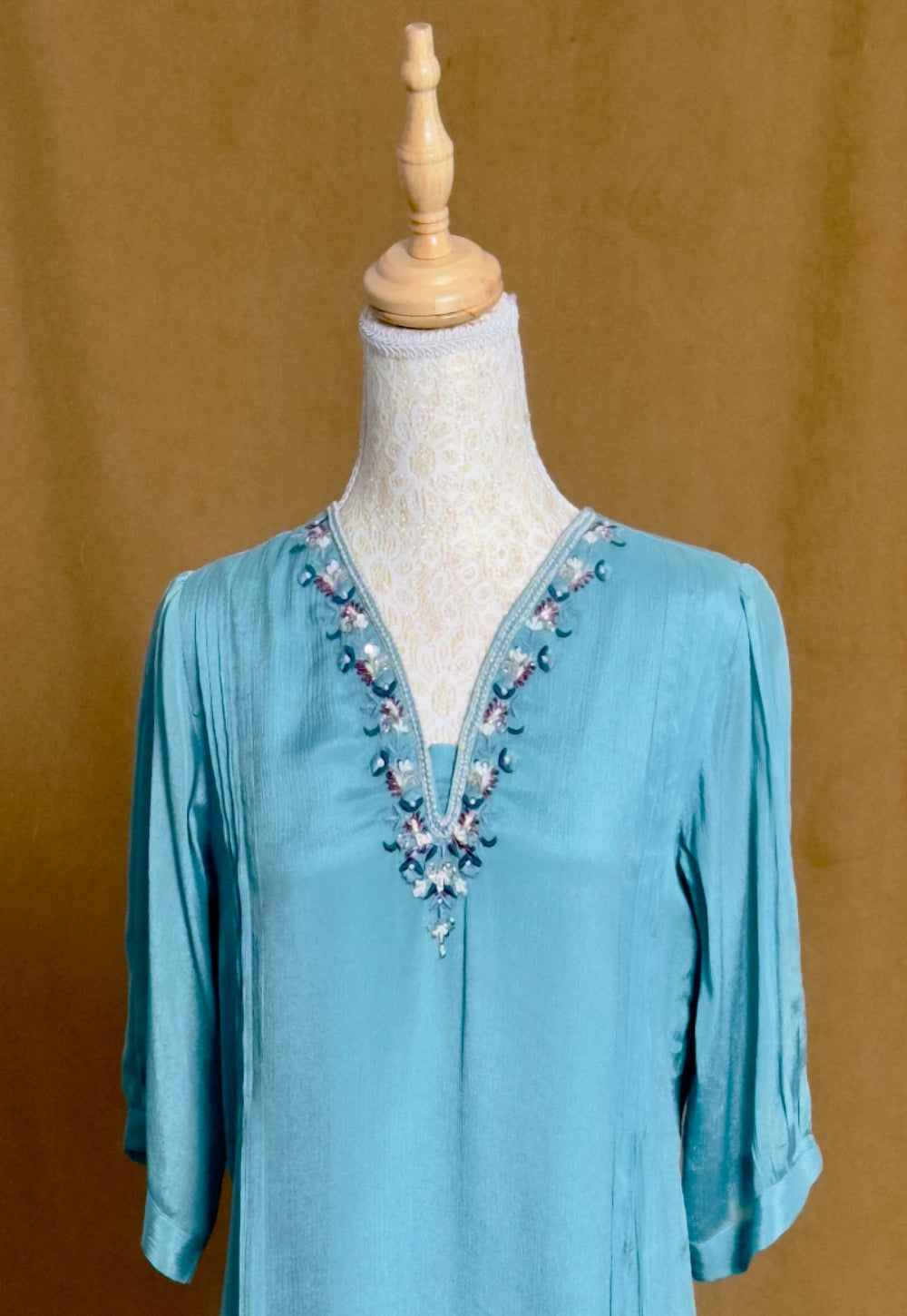 Blue blouse with floral embroidery on a mannequin against a brown background