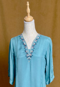Blue blouse with floral embroidery on a mannequin against a brown background