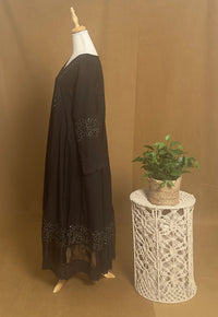Black dress on a mannequin next to a small plant on a decorative stand against a brown background