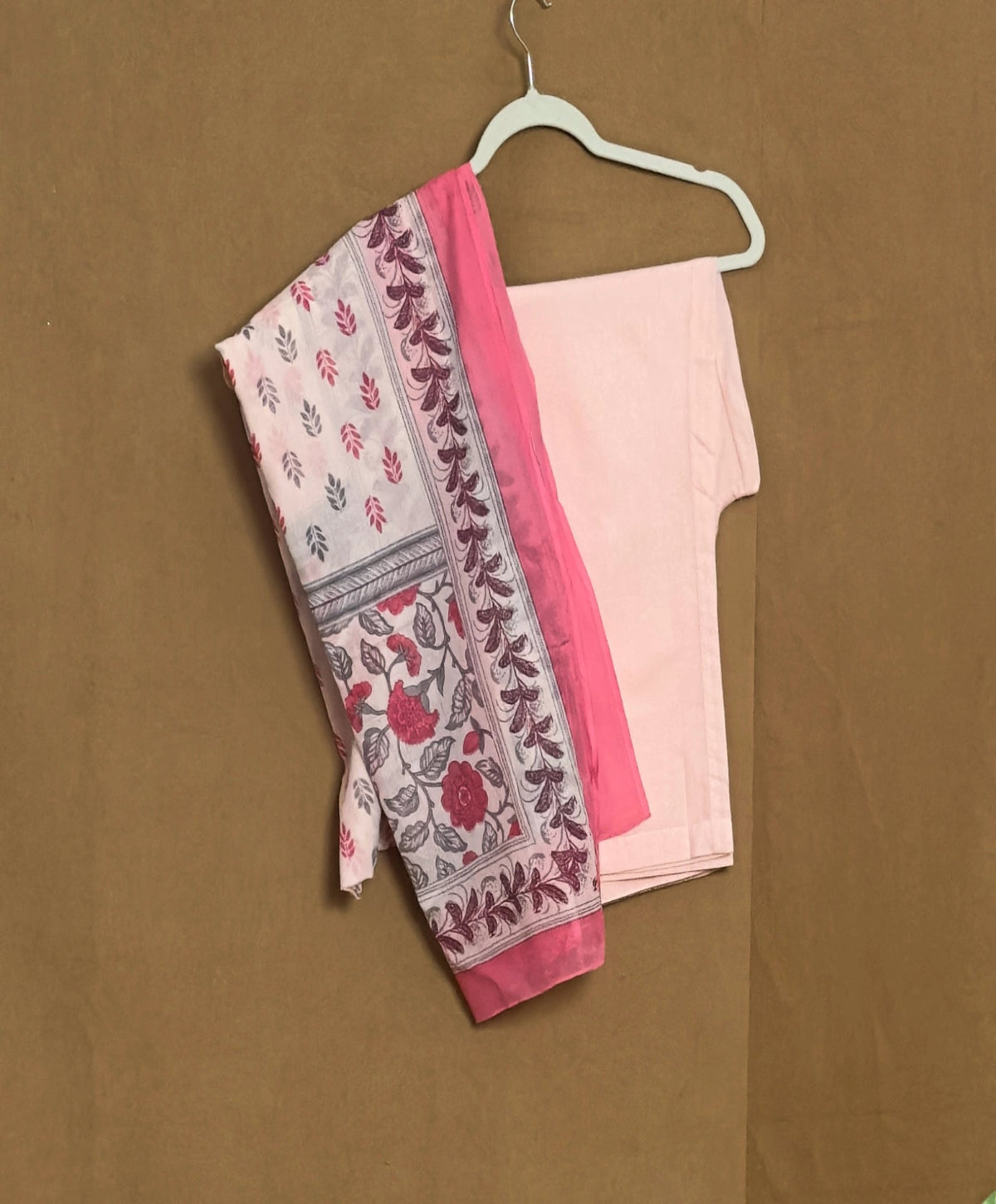 Pink saree with floral patterns on a hanger against a brown background