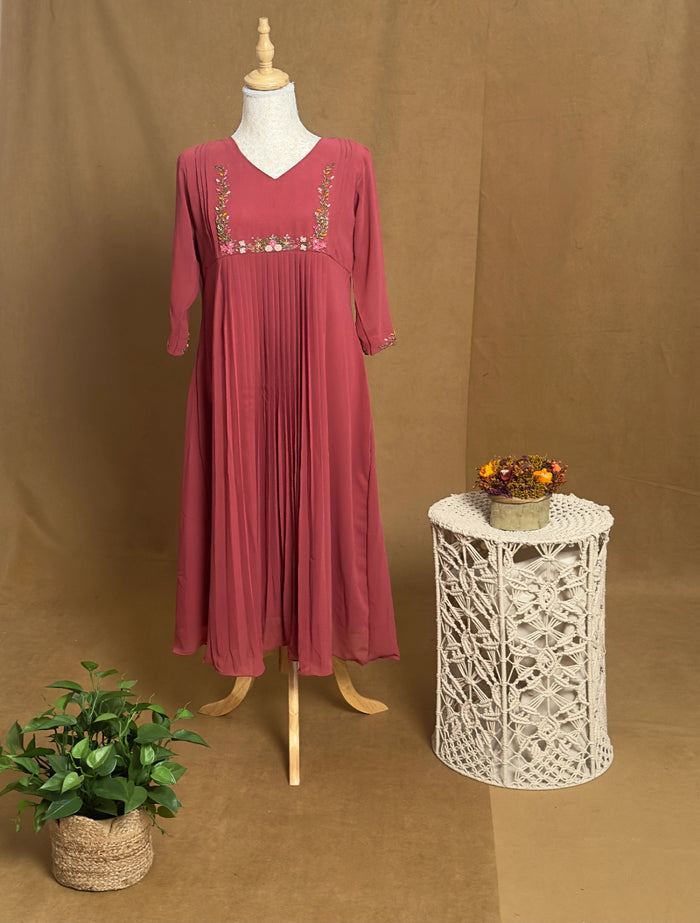 Pink dress on a mannequin against a brown background with a small table and plant.