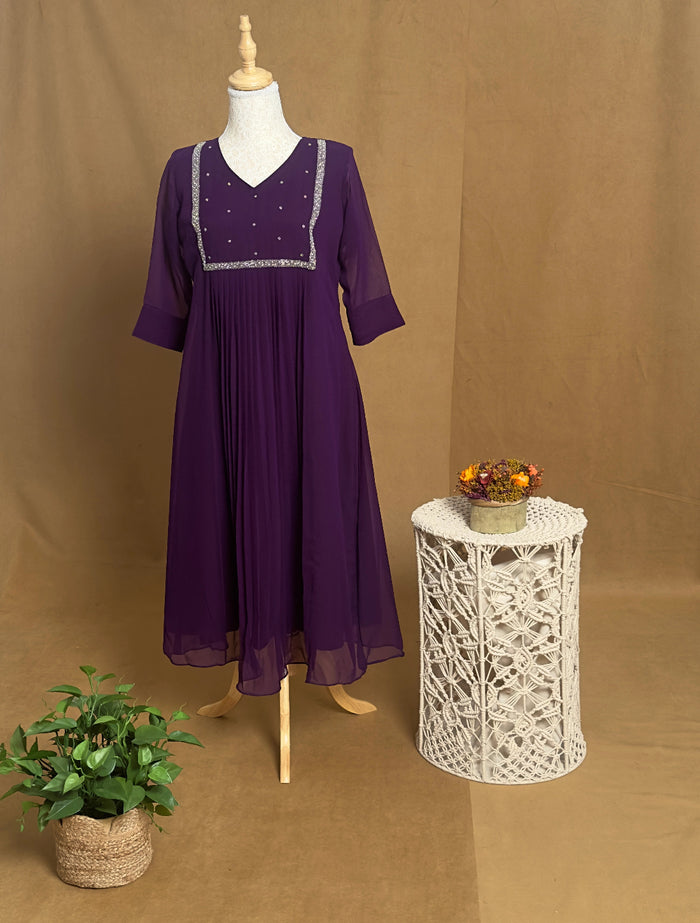 Purple dress on a mannequin with a small table and plant against a brown background