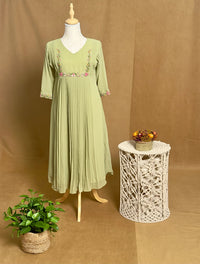 Green dress on a mannequin with a small table and plant against a brown background
