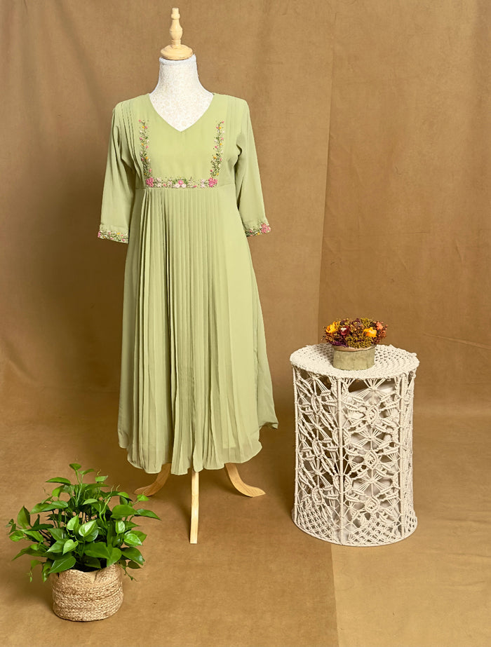 Green dress on a mannequin with a small table and plant against a brown background