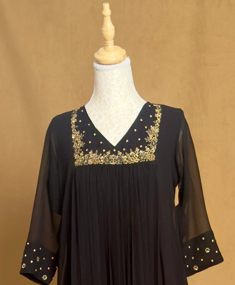 Black dress with gold embroidery on a mannequin against a beige background