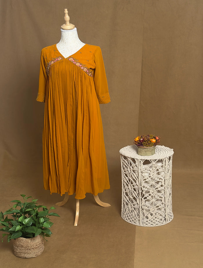 yellow dress on a mannequin with a white lace table and plant against a brown background