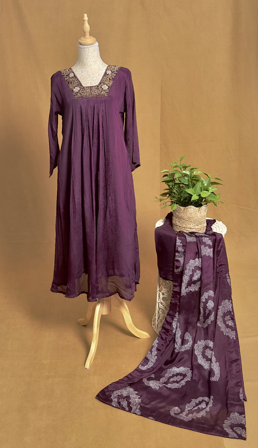 Purple dress on a mannequin with a matching scarf draped over a chair against a brown background
