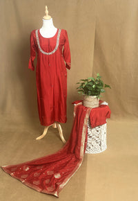 Red embroidered dress on a mannequin with a matching fabric draped over a table against a brown background