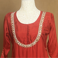 Red dress with gold embroidery on a mannequin against a brown background